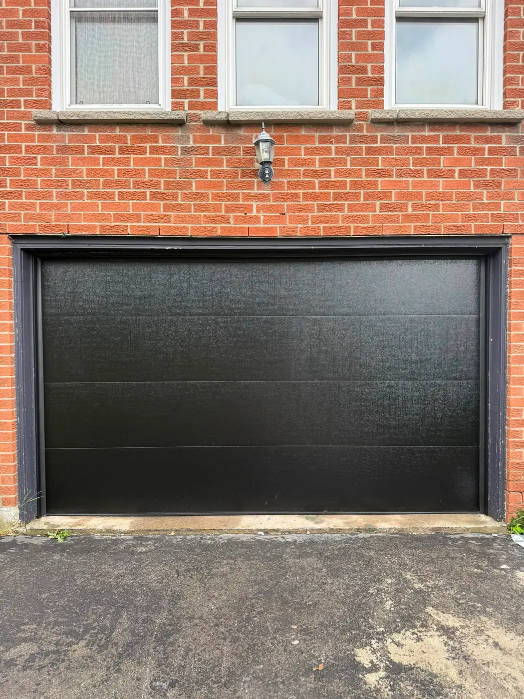 Black flush-panel double garage door on a red brick home — GTA