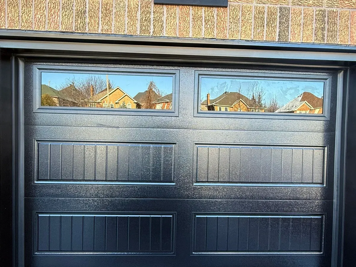 Black flush-panel garage door on stone home — Oakville