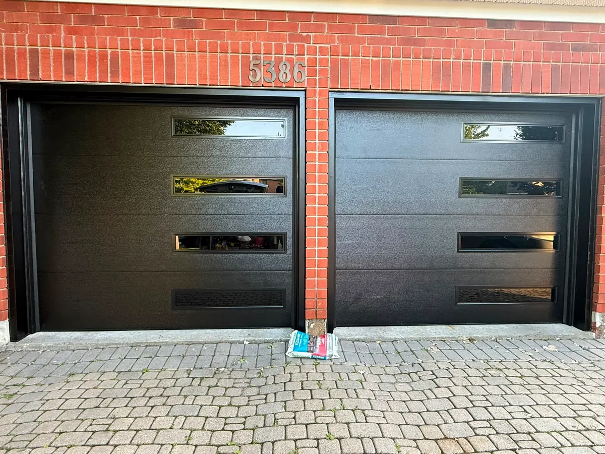 Pair of black modern flush-panel single garage doors on a red brick home — GTA