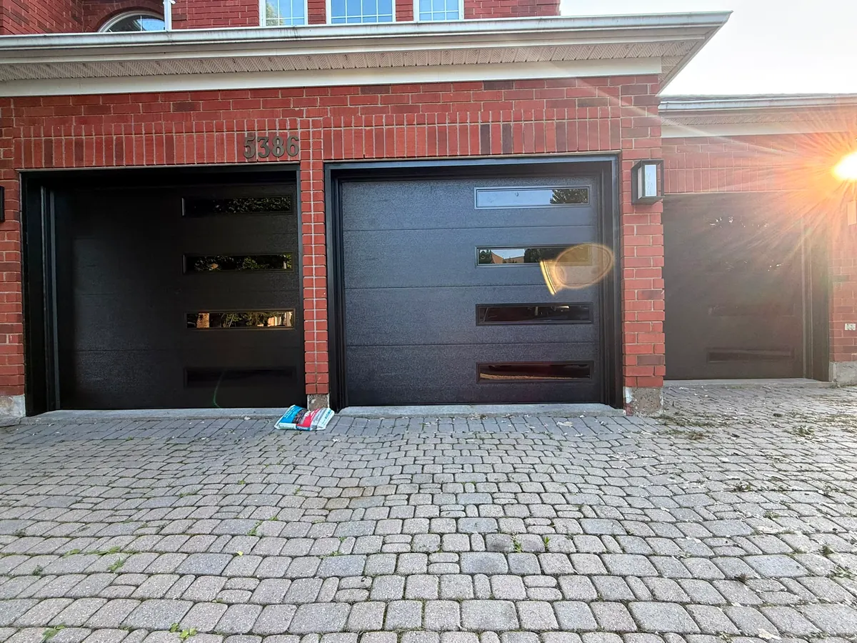 Two black modern flush-panel single garage doors on a brick home — GTA