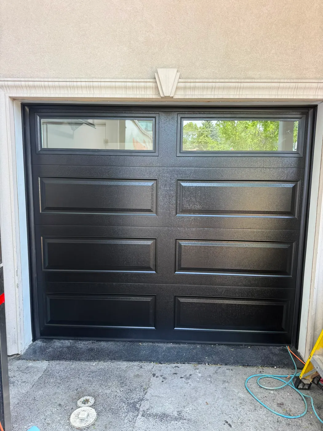 Black raised-panel single garage door with top windows on a stucco home — GTA