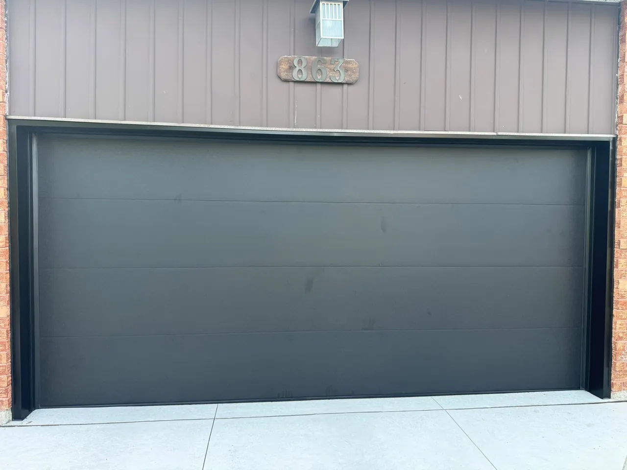 Dark charcoal modern flush-panel garage door on a home with brown siding — GTA