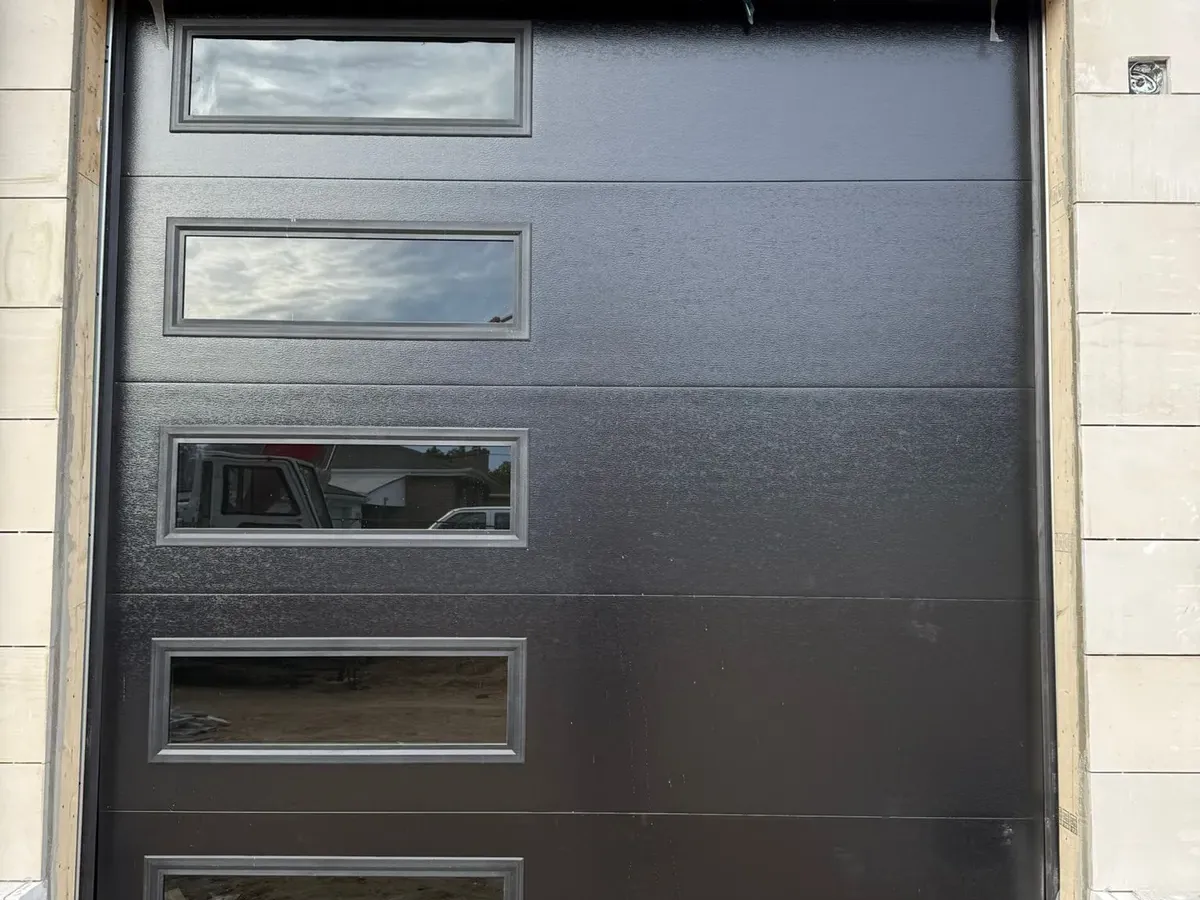 Dark charcoal modern flush-panel garage door on a stone home
