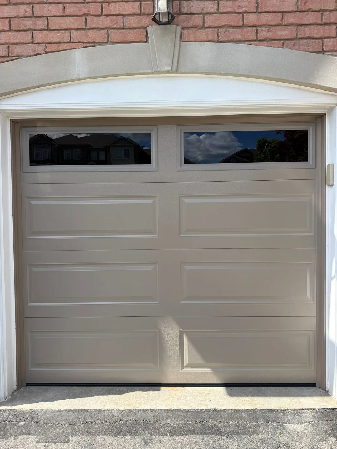 Tan raised-panel garage door with an arched brick surround — GTA